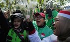 Ride hailing drivers shout slogans as they hold flowers during a peace rally in Jakarta, Indonesia.