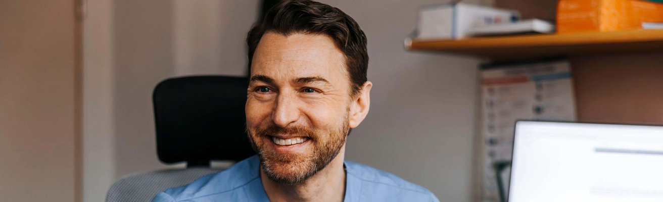 Happy male medical expert holding ear thermometer while talking with patient in examination room