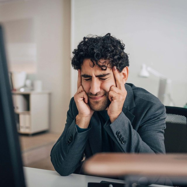 Stressed male entrepreneur touching temples while sitting at desk in creative office