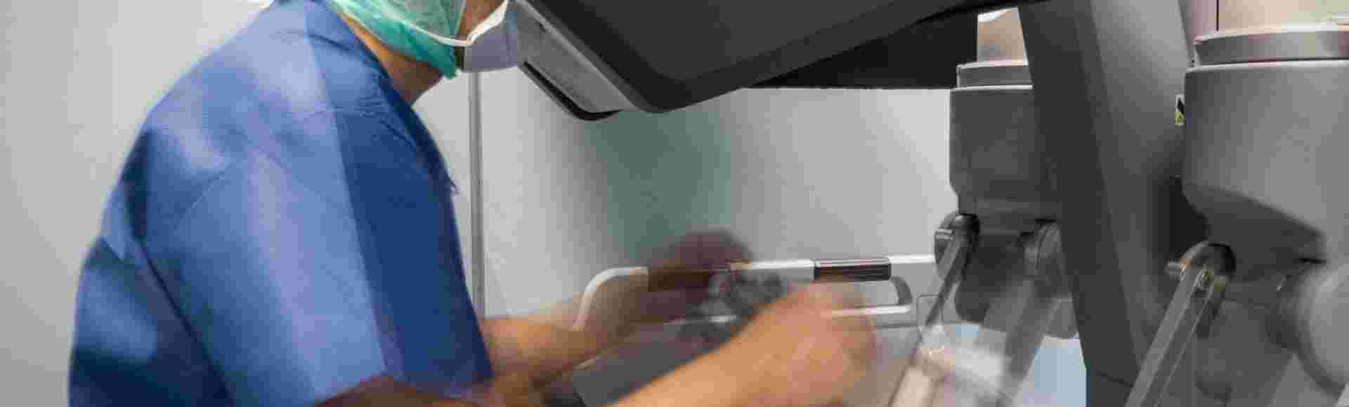 A surgeon manipulates the controls of a robot that operates on a patient.