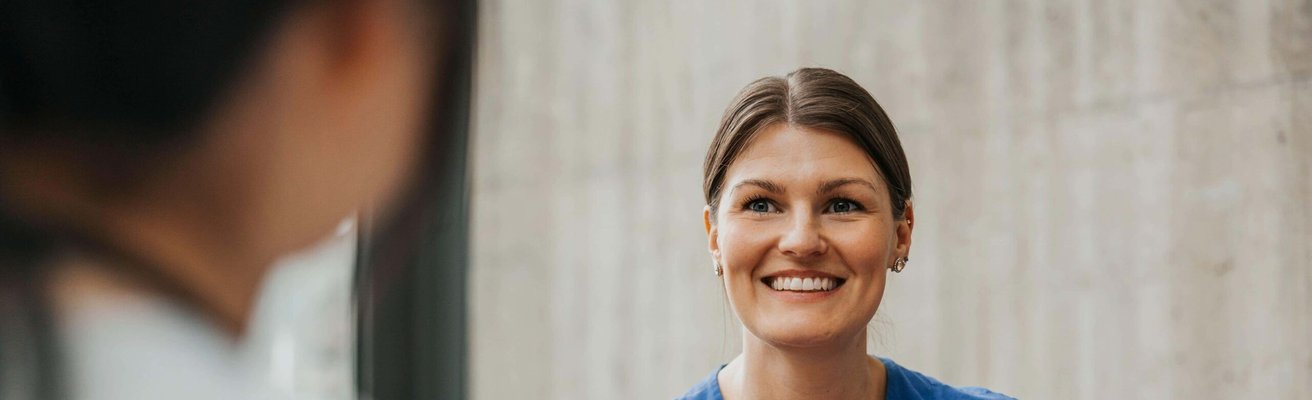 Smiling female physician wearing medical scrub talking with coworker in hospital lobby
