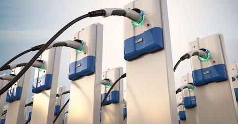 A close-up picture of EV chargers with the sun shining on the blue skies in the background.