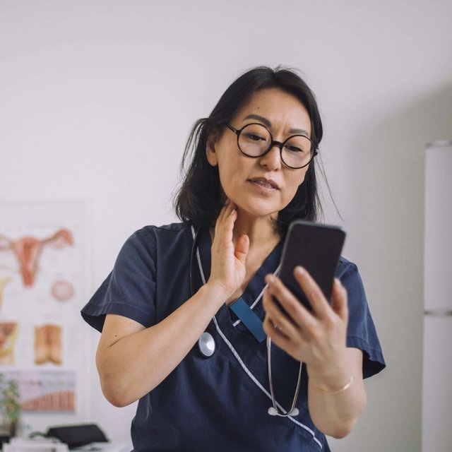 Female otolaryngologist doing online consultation through mobile phone while sitting at desk in medical clinic