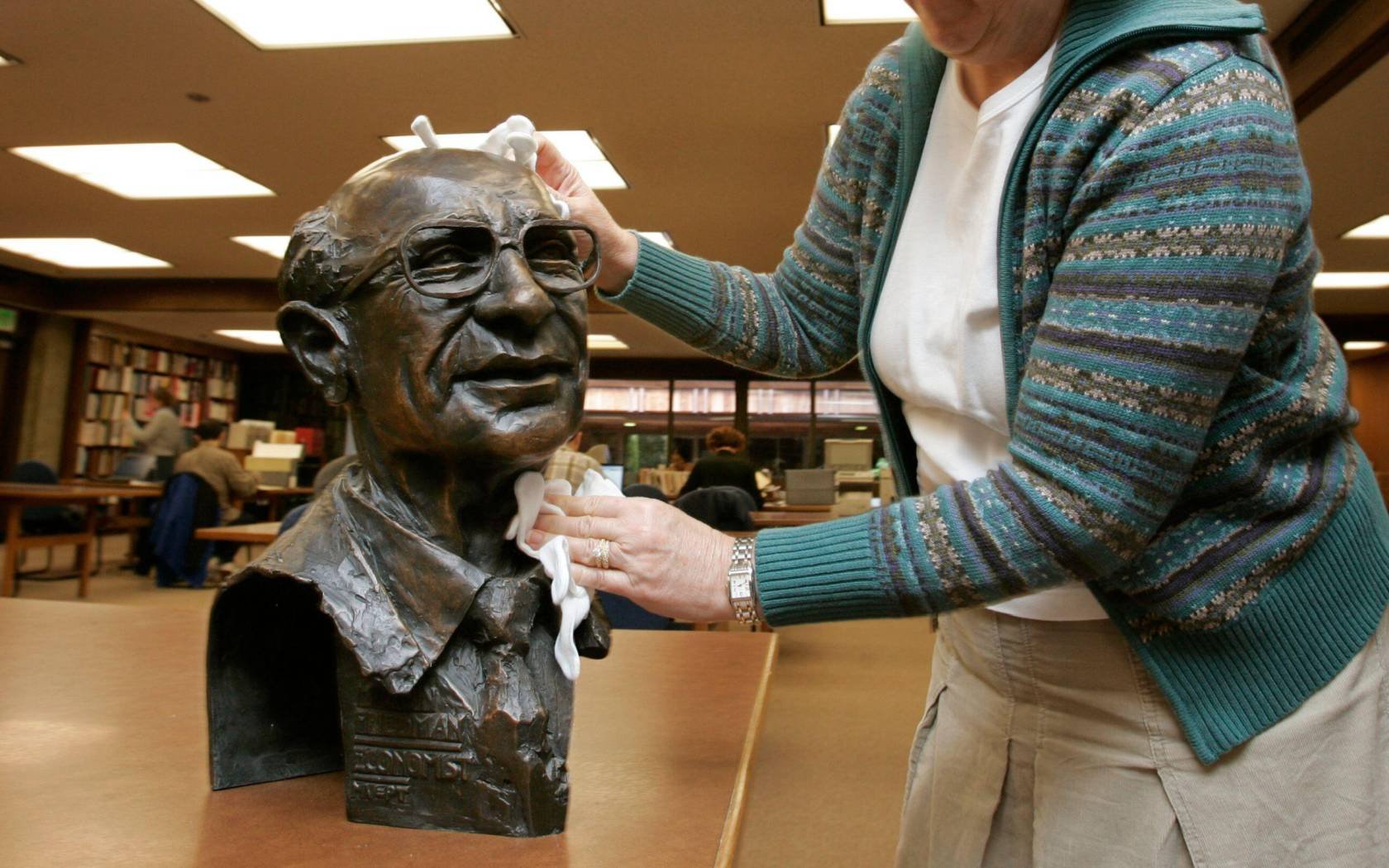 An archivist polishes a sculpture of Milton Friedman.