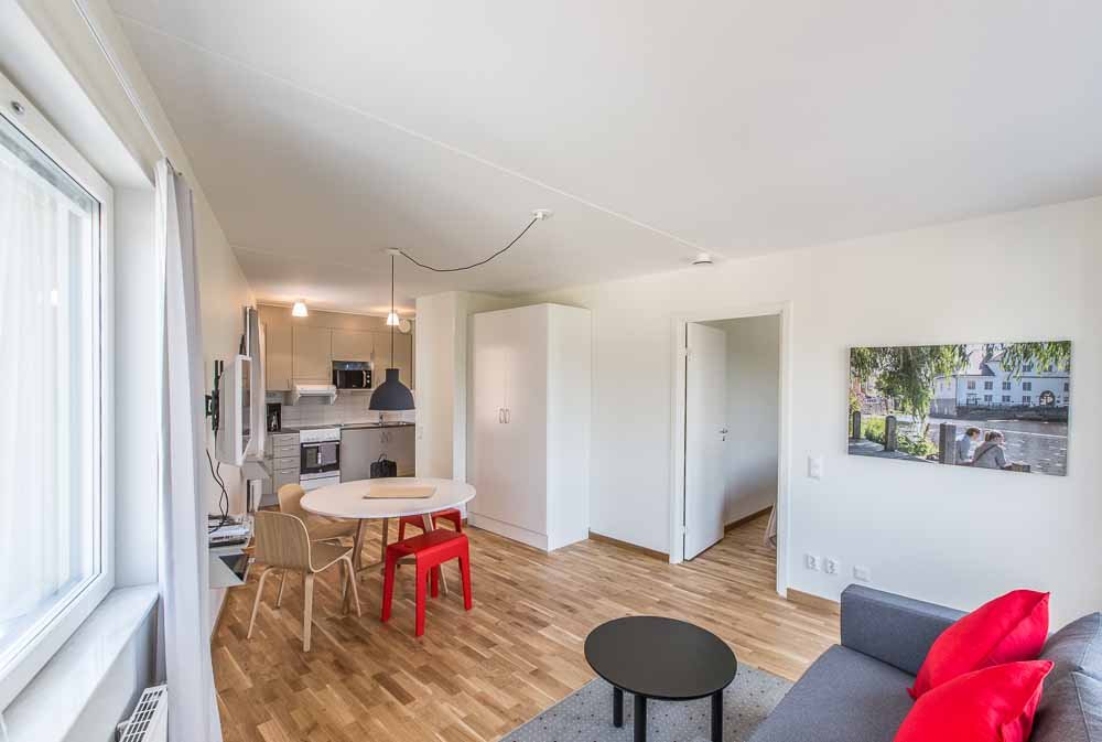 Apartment with white walls, couch, coffeetabel, wardrobes a round table and chairs. Kitchen with stove, oven microwave and cupboards.