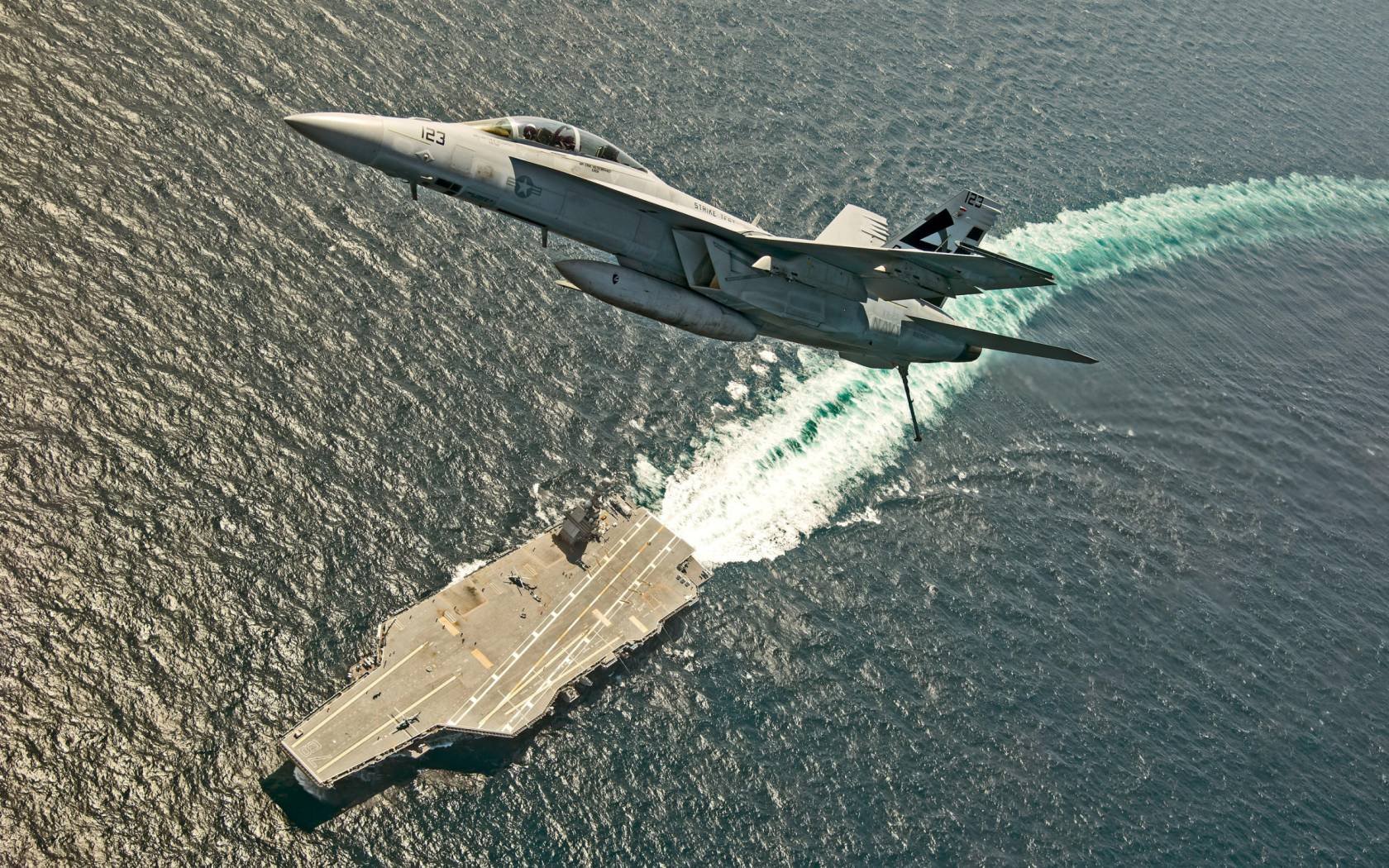 A US Navy F/A-18F Super Hornet jet fighter aircraft flies over the USS Gerald R. Ford.