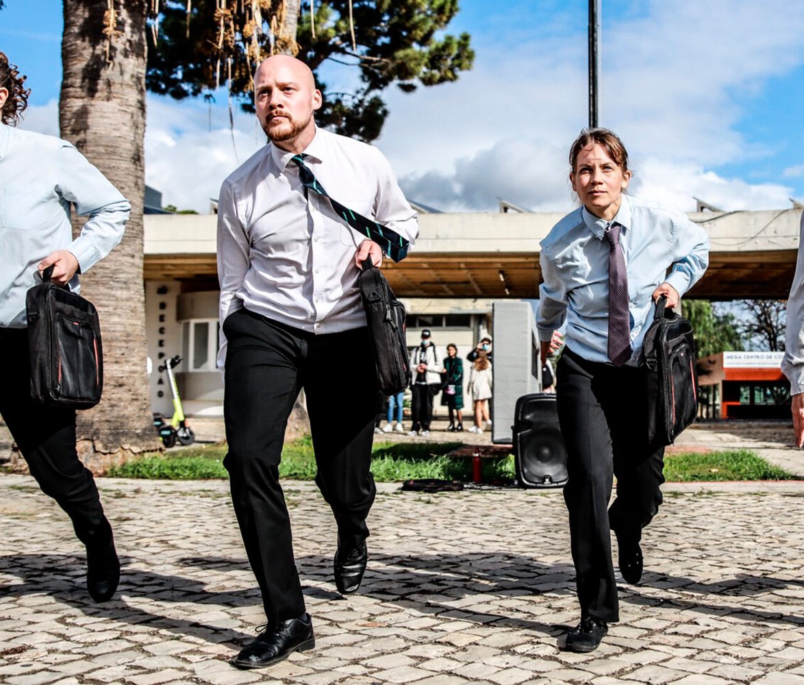 Fyra dansare med kostymbyxor, skjorta och slips med portföljer i händerna.