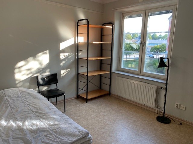 Studentn room with bed chair, bookshelf and floorlamp.