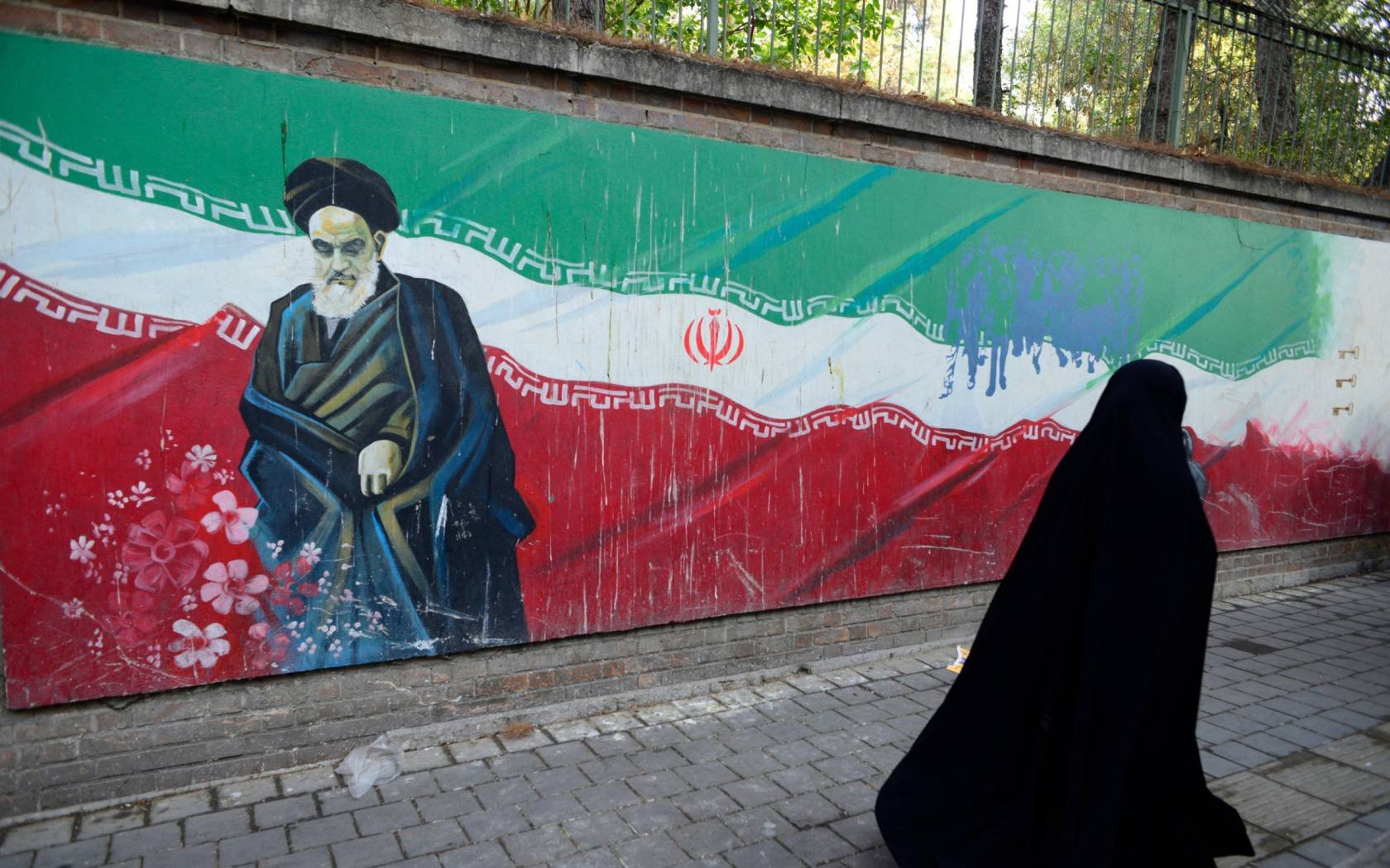 A veiled Iranian woman walks past a mural of Ayatollah Khomeini on a wall of the former US Embassy in Tehran, Iran