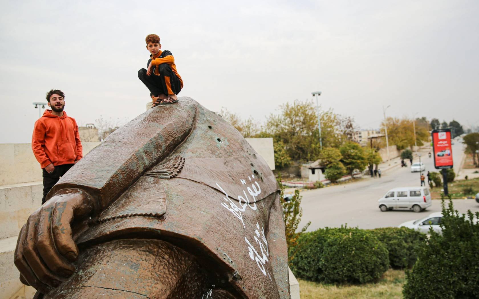 Children sit on a broken statue of former Syrian President Hafez al-Assad.
