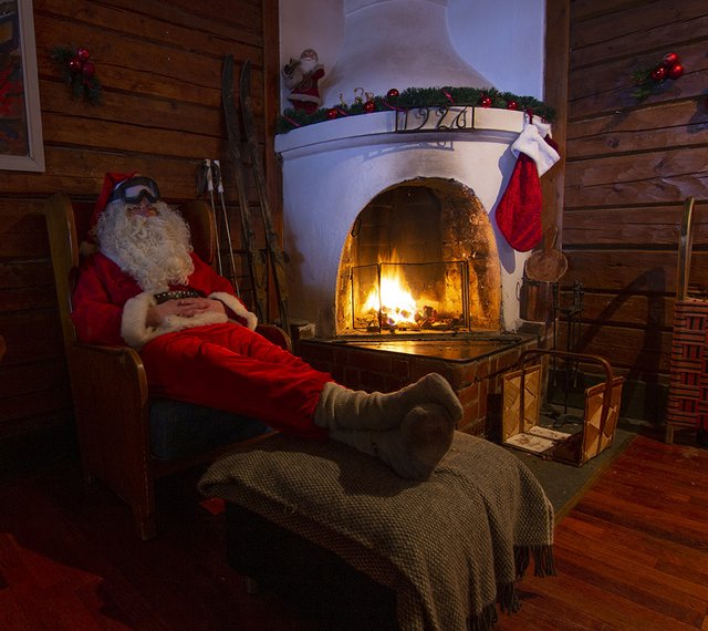 Jultomten i sin ski lodge sover i en fåtölj vid den öppna elden med skidglasögon på pannan.