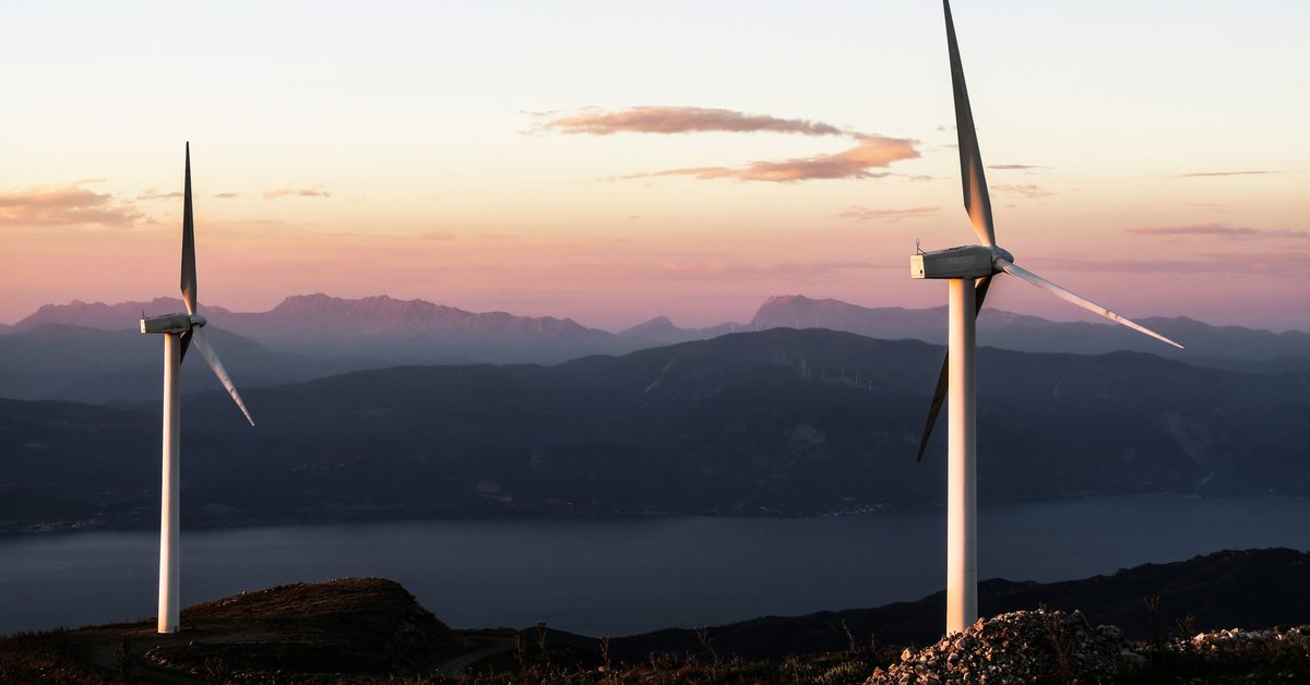 Two wind turbines stand out in front of a beautiful background of mountains during sunset.