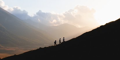 Tre personer bestiger et fjell i morgentåken.
