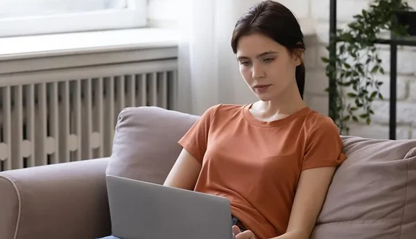 Nainen istuu sohvalla tietokoneensa kanssa.
