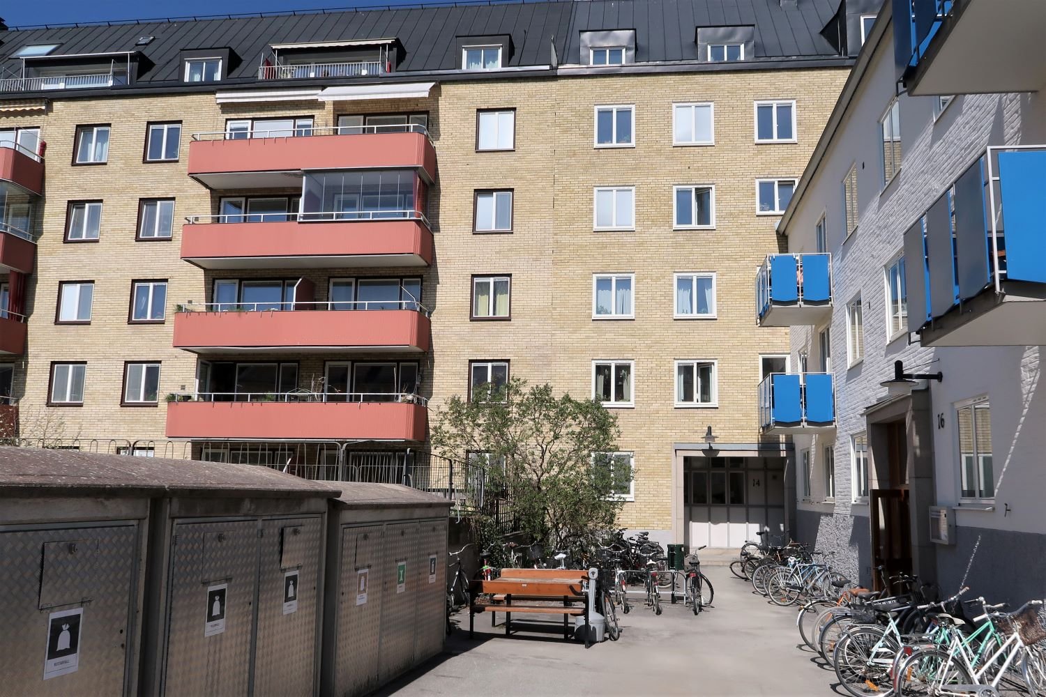Exterior of yellow brick building with recycling facilities and bicycle parking outside.