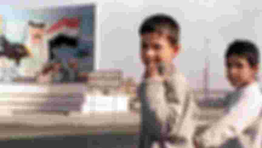 Iraqi children in front of a mural of Saddam Hussein, Baghdad, 1999. Credit: KARIM SAHIB/AFP via Getty Images.