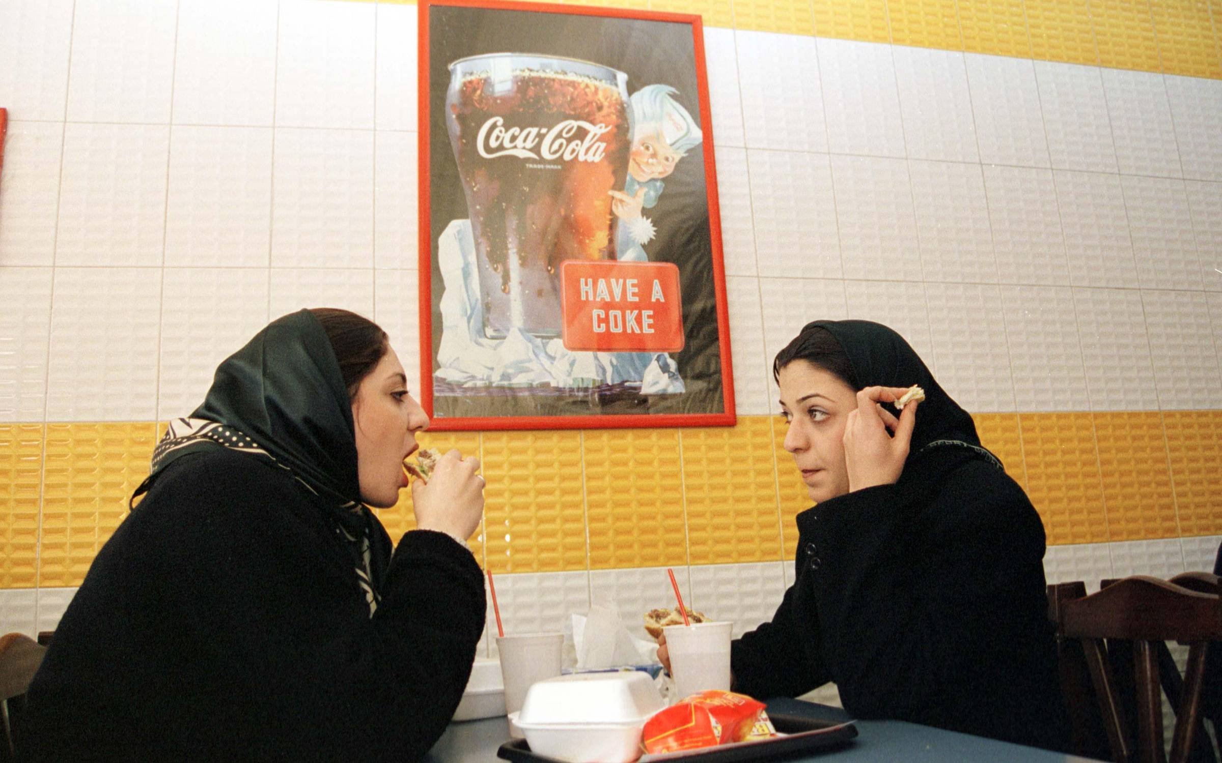 Two young women in veils enjoy a hamburger