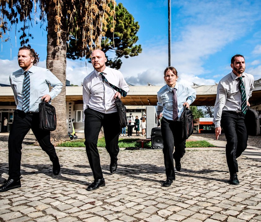 Fyra dansare med kostymbyxor, skjorta och slips med portföljer i händerna.