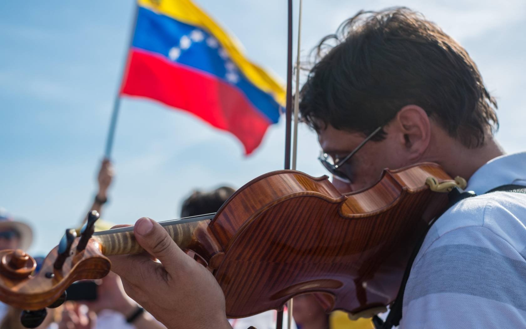 A violinist plays in front of a Venezuelan flag.