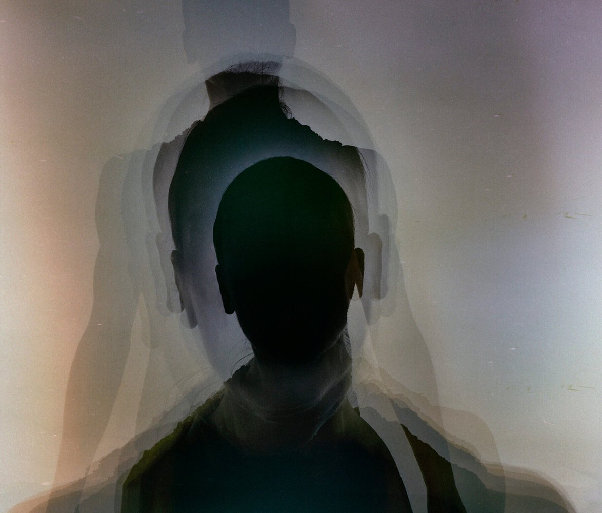 Silhuett av en person med flera överlappande konturer som skapar en suddig, nästan ekoliknande effekt runt huvudet och axlarna. Bilden har dämpade toner i grått, svart och svagt beige, vilket ger ett drömskt och abstrakt uttryck.