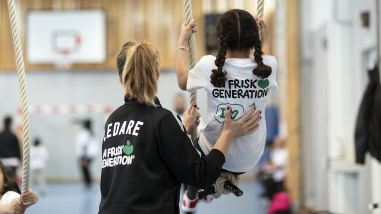 Gruppledare hjälpler en flicka i gympasalen som utöver hälsofrämjande aktiviteter