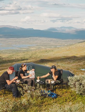 tv&aring; kvinnor och en &auml;ldre herre &auml;ter middag p&aring; fj&auml;llet vid sitt t&auml;lt