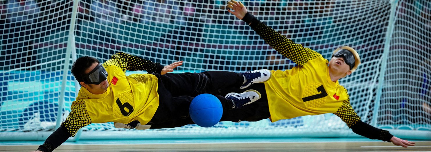 Två målvakter i goalball slänger sig åt varsitt håll och räddar bollen.