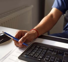 Male healthcare worker holding pen near keyboard at desk in hospital