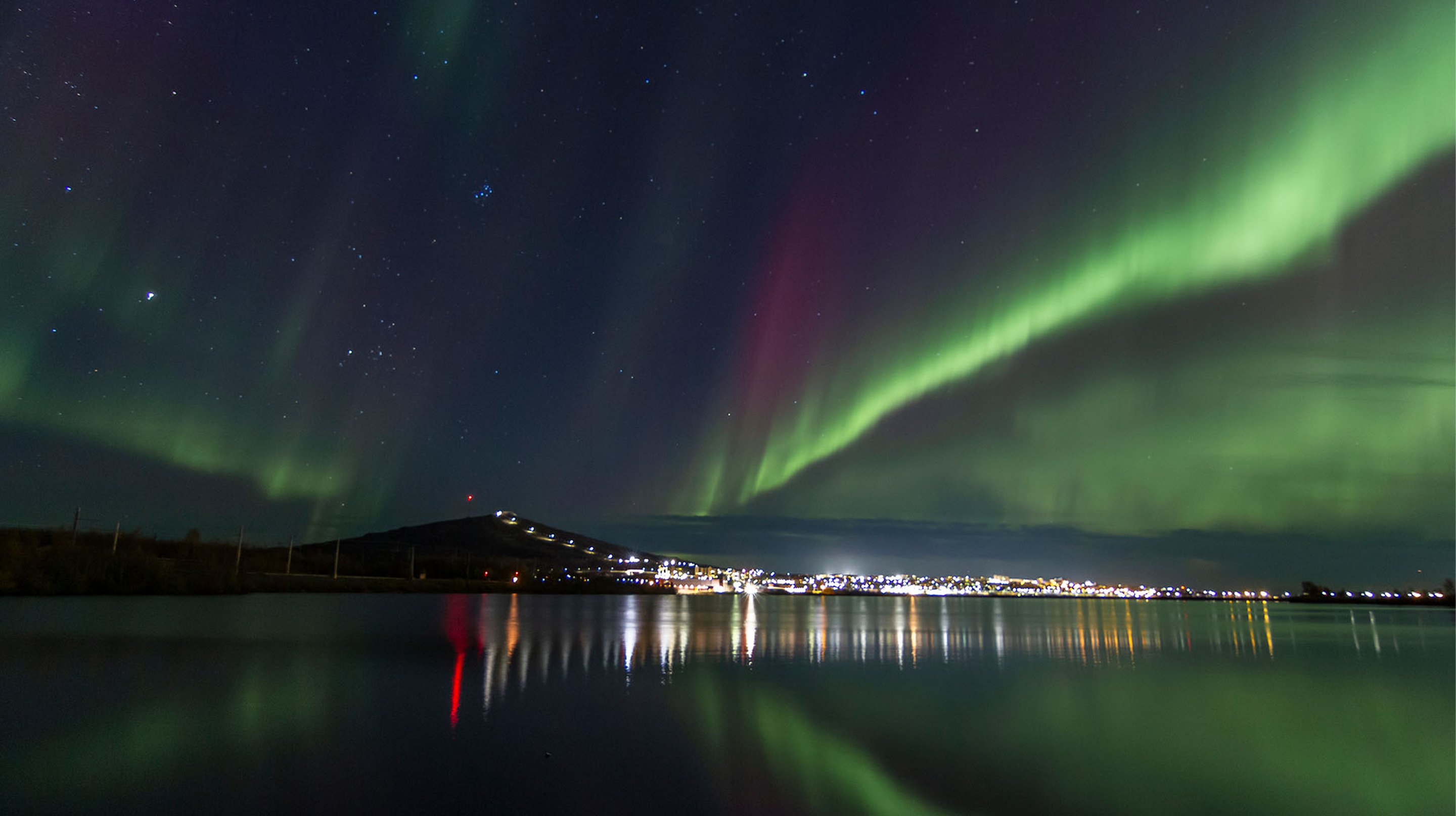 Norrsken över Kiruna stad med reflektioner i sjön framför.