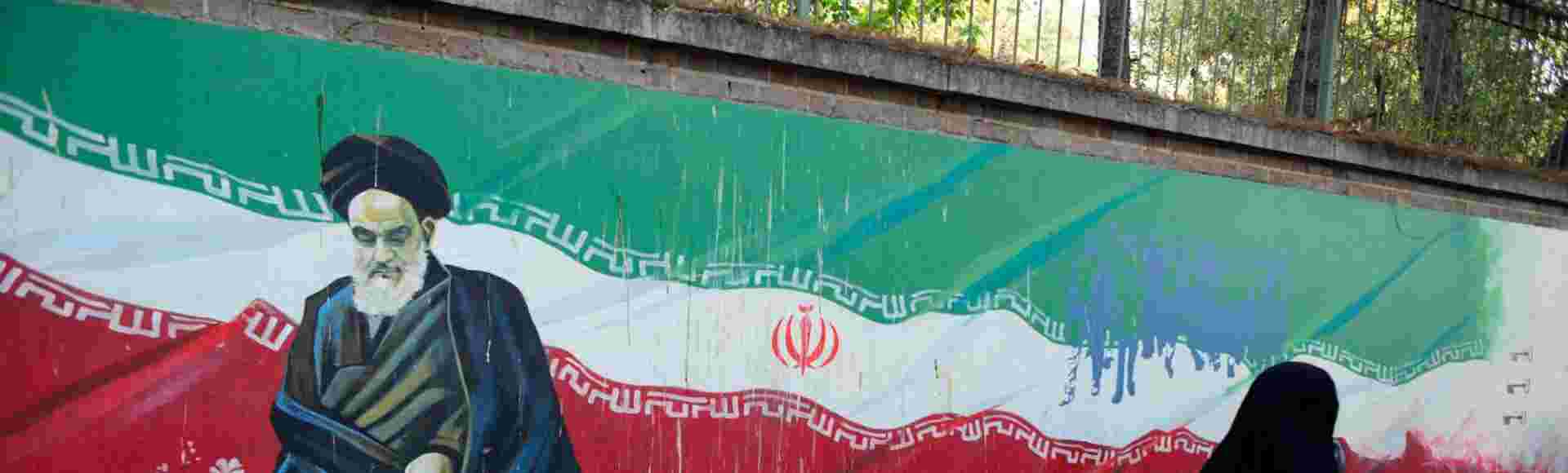 A veiled Iranian woman walks past a mural of Ayatollah Khomeini on a wall of the former US Embassy in Tehran, Iran