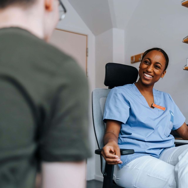 Smiling young medical expert sitting near computer and talking with patient in doctor's office