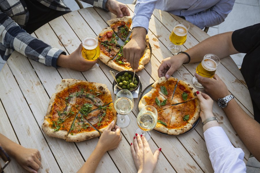 Flera h&auml;nder som str&auml;cker sig efter pizza och oliver