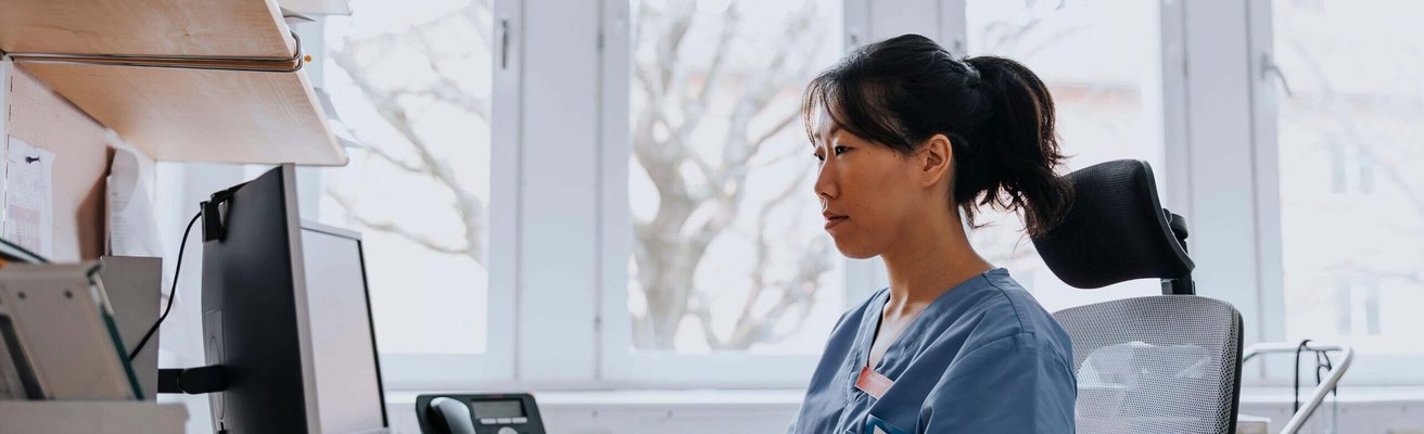 Female healthcare worker working on computer while sitting in examination room at hospital