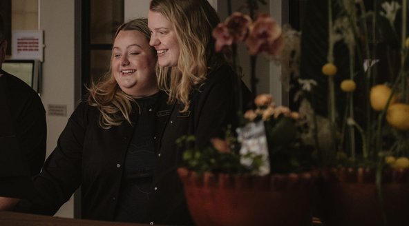 Två receptionister som skrattar och hjälps åt 