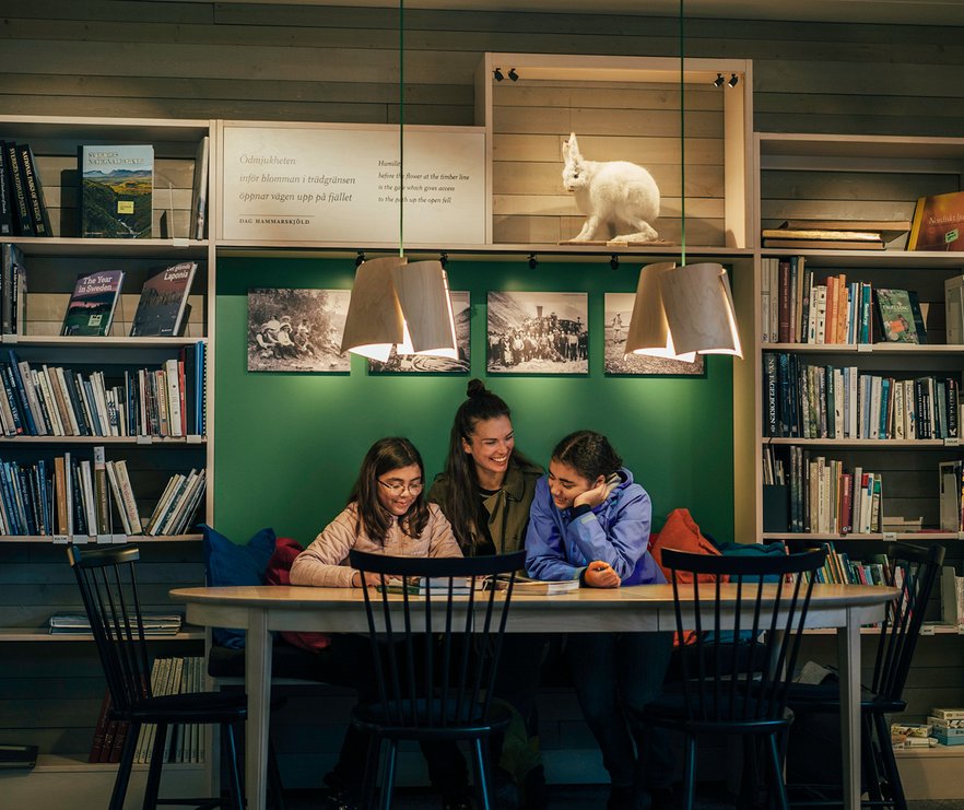 en mamma med sina d&ouml;ttrar l&auml;ser i biblioteket p&aring; Naturum i Abisko