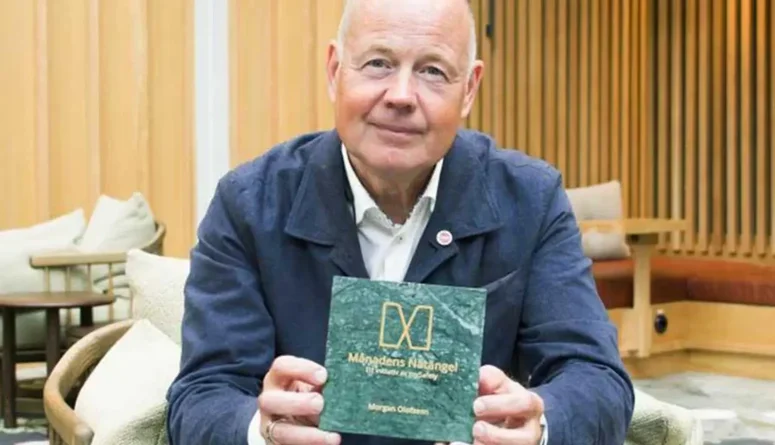 Morgan Olofsson sitter i en lobby och håller i priset för månadens Nätängel.