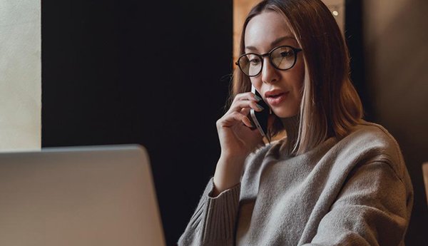 Nainen puhuu puhelimessa samalla kun käyttää tietokonetta.