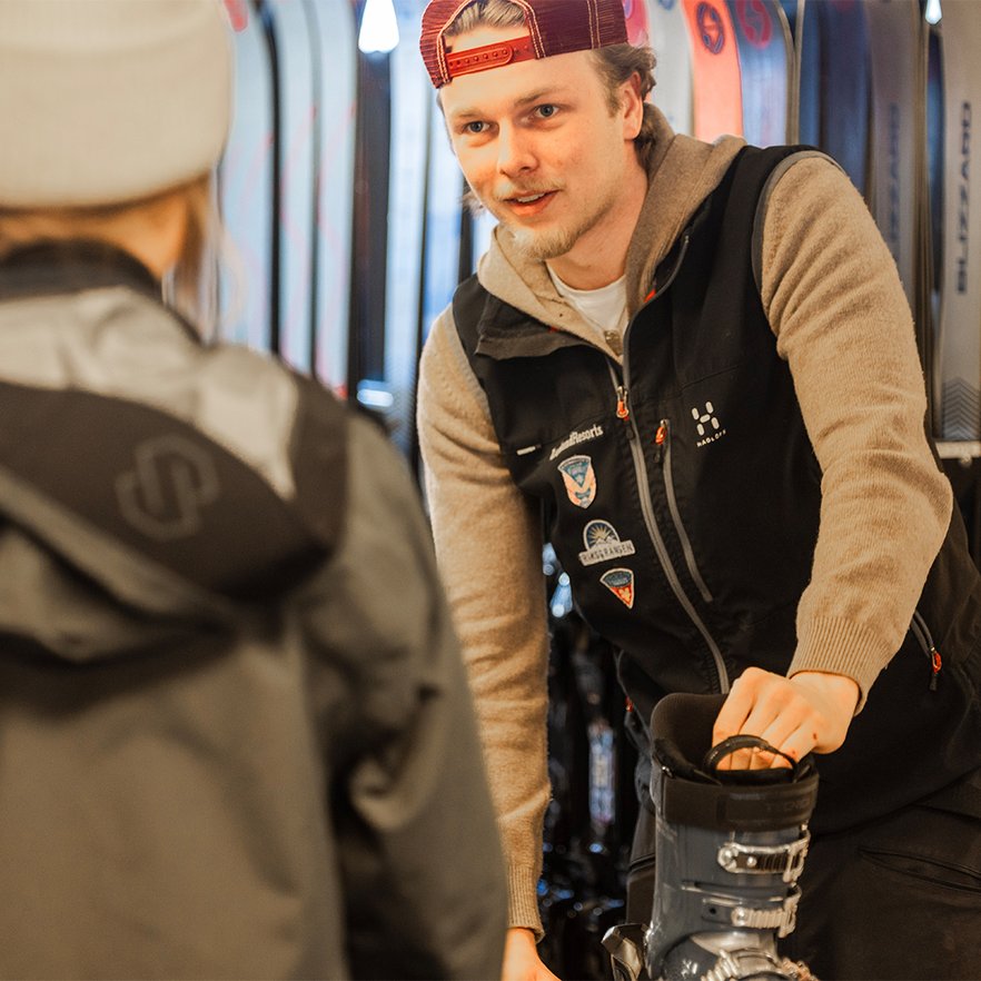 en sportshopmedarbetare hj&auml;lper en g&auml;st med skidutrustning