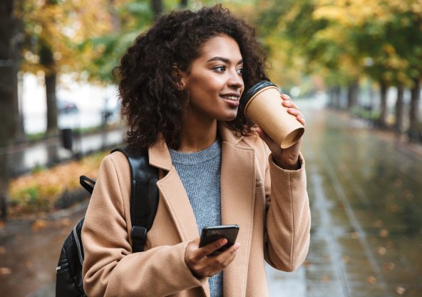 Ung kvinna i park med mobil och kaffemugg