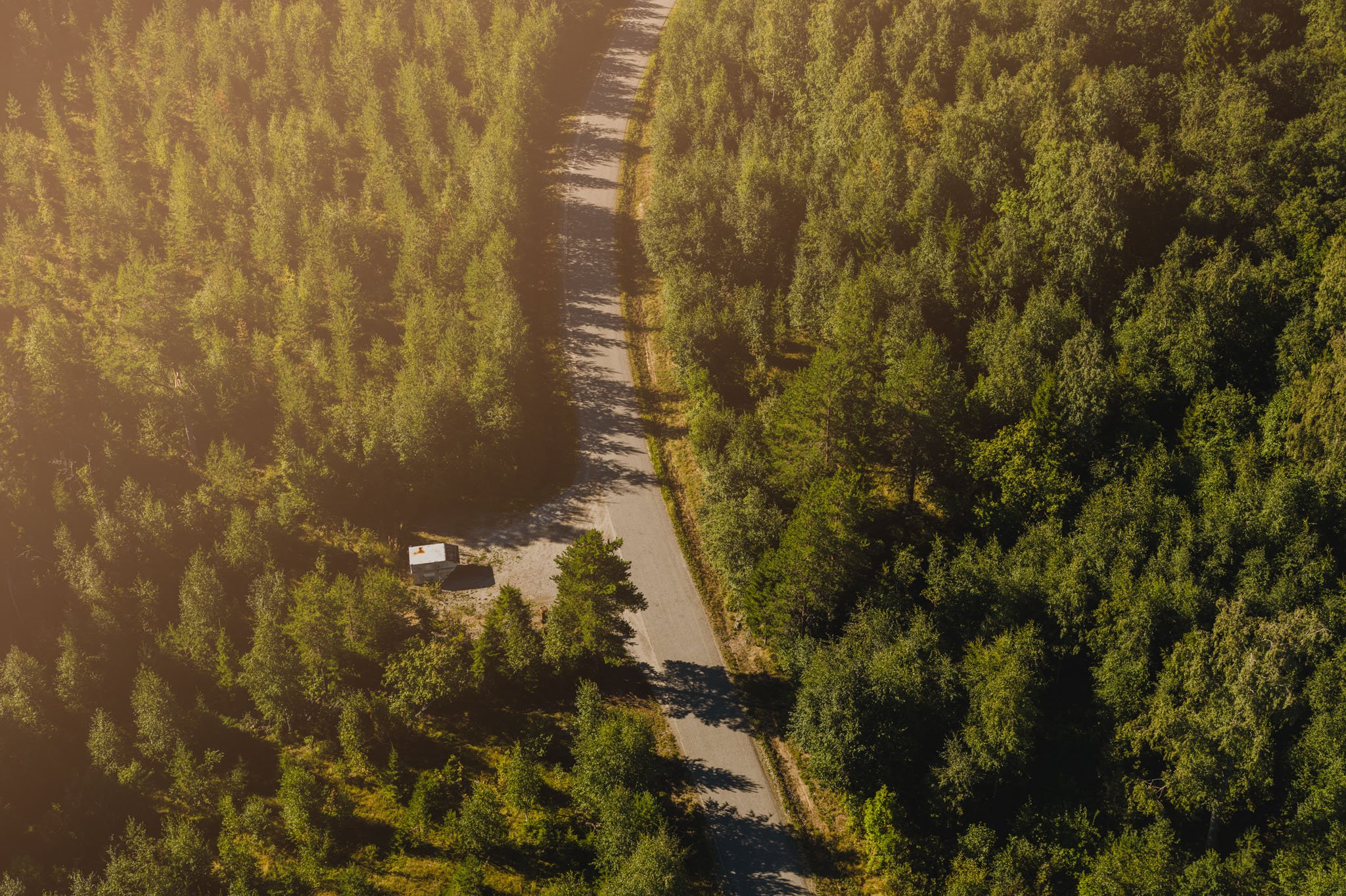 Flygfoto &ouml;ver t&auml;t barrskog med b&auml;ck och ett litet hus vid vattnet.