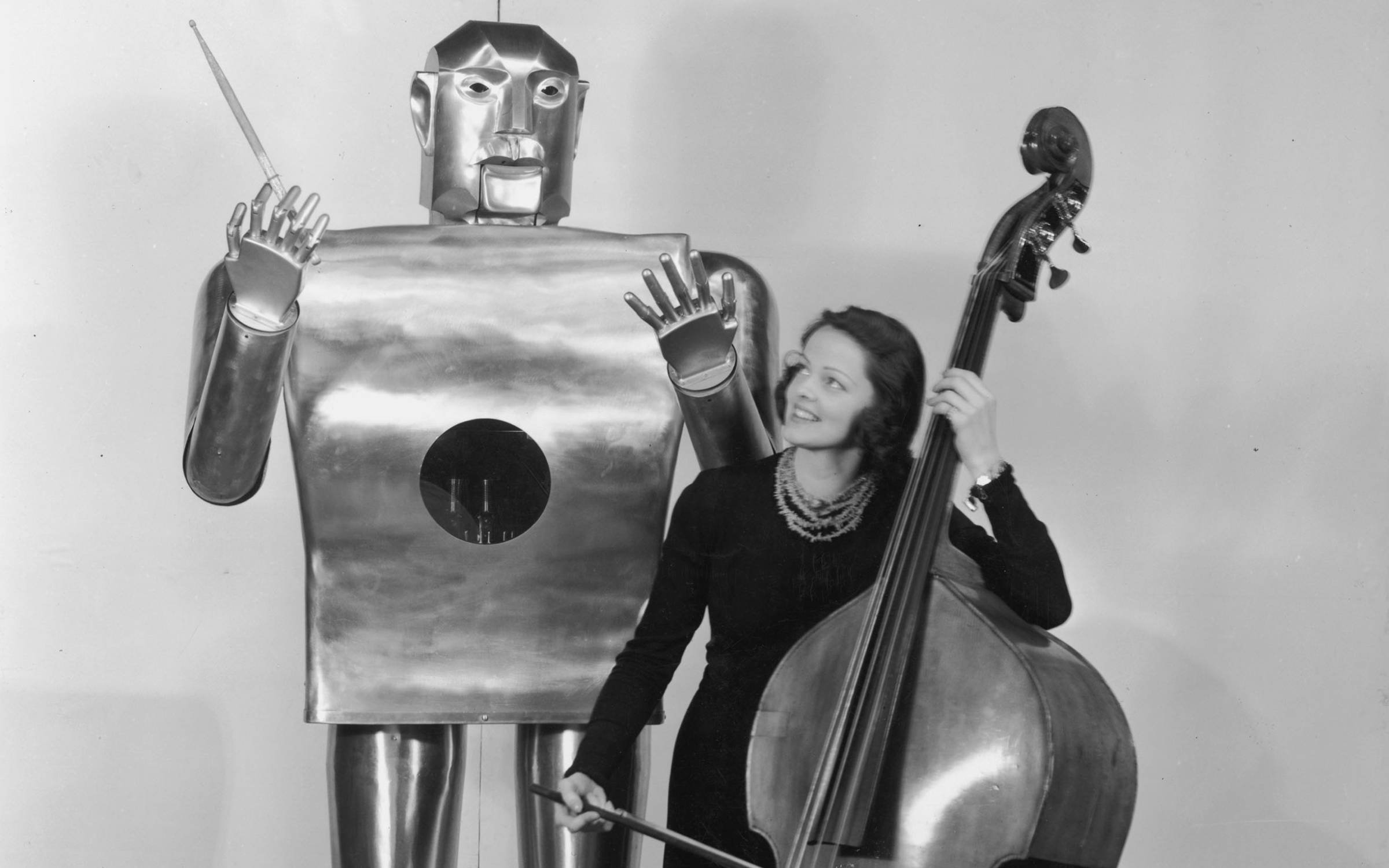 Musician Lois Kendall plays the cello while a mechanical man named Elektro 'conducts' on stage as part of a Westinghouse Electric and Manufacturing Co demonstration at the World's Fair, New York City, 1939