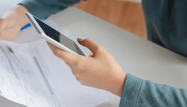 En person håller i en faktura samtidigt som den skriver på telefonen.