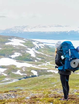 A woman looks out over a snow-dotted mountain heath with her hiking backpack on her back in Björkliden
