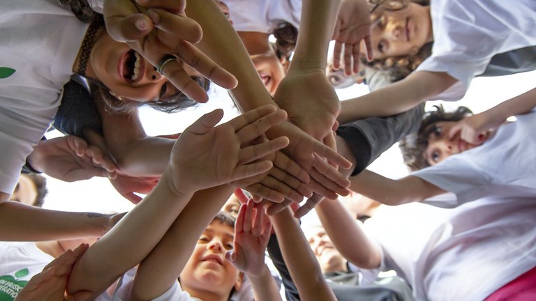 Barn står i en ring och lägger händerna över varandra i en aktiv gemenskap.