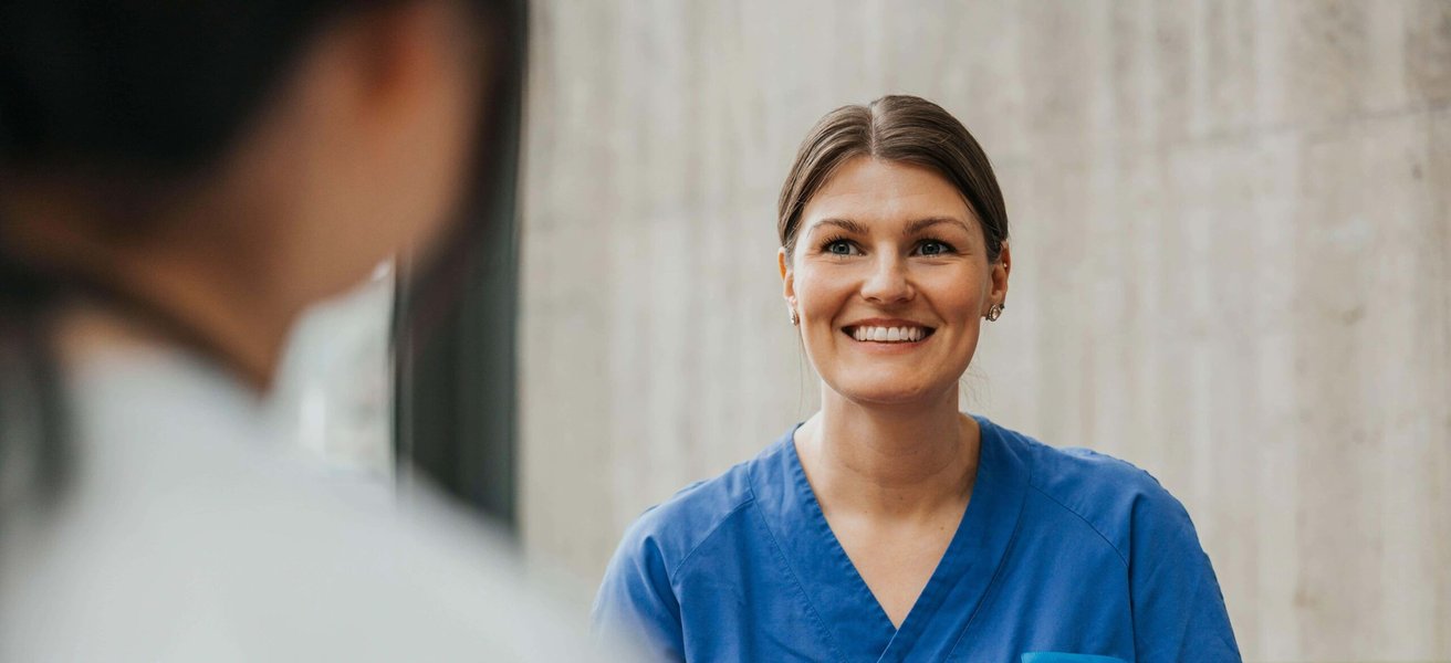 Smiling female physician wearing medical scrub talking with coworker in hospital lobby