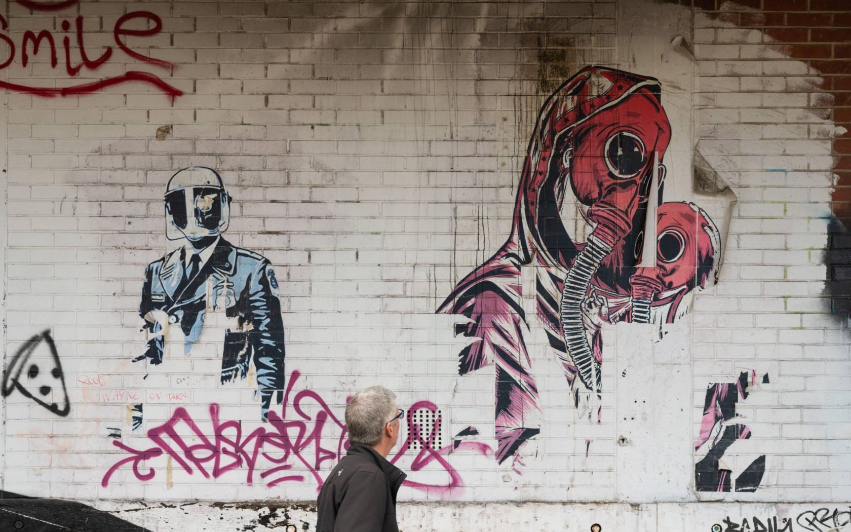 A man walks past mural which connects gas masks and the Covid pandemic.