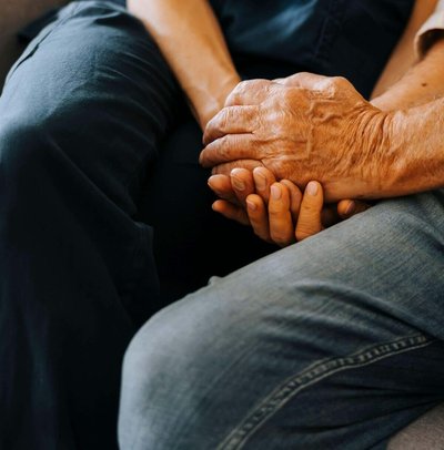 Midsection of senior male holding hands of female caregiver while sitting on sofa at nursing home