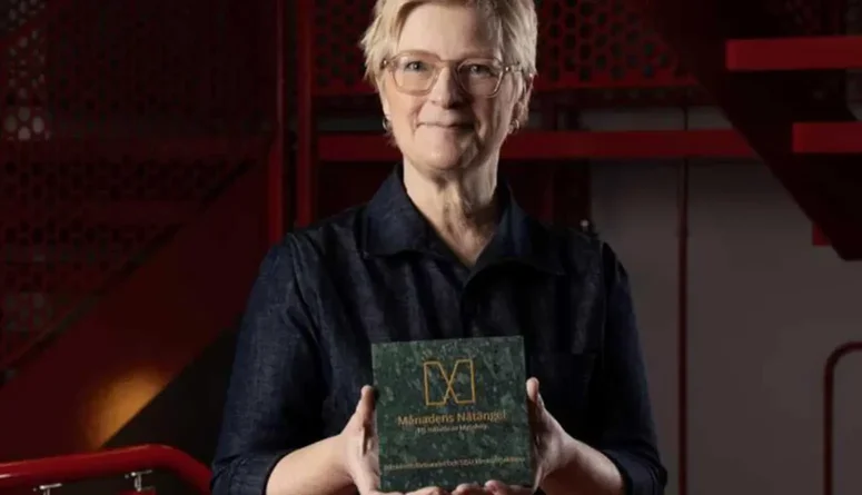 Anna Iwarsson står vid en röd trappa och håller i priset för månadens Nätängel.