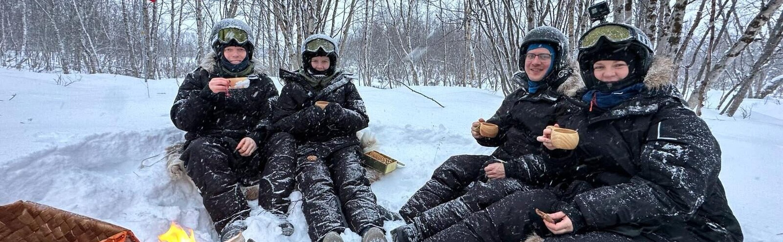Guests enjoying a traditional outdoor fika by the fire during a guided snowmobile tour in Abisko, Swedish Lapland.