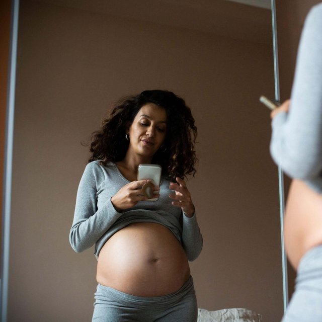 Reflection of pregnant woman taking selfie on smart phone at home